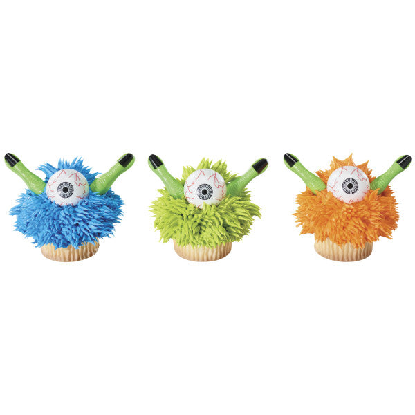 Three decorated cupcakes with blue, green, and orange monster designs using eyeball and finger picks.