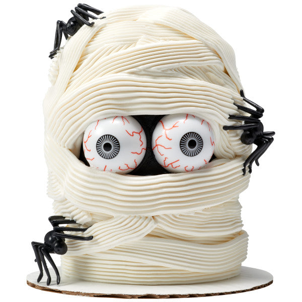 Mummy cake design featuring two eyeball picks peeking through piped white frosting and plastic spiders.
