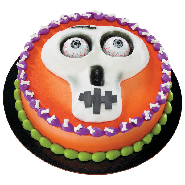 Round Halloween cake with fondant skull face and two eyeball picks as eyes.
