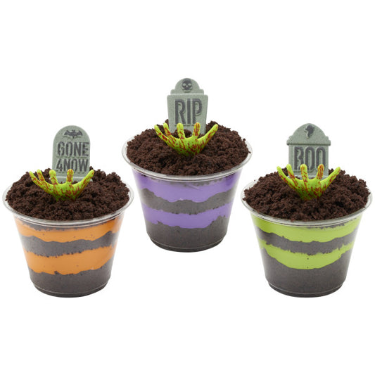 Halloween pudding cups topped with dirt crumbs, tombstone toppers, and zombie hand picks reaching out of the “ground.”