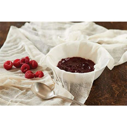 Cheesecloth draped over a bowl filled with raspberry jam, fresh raspberries and a spoon beside it on a wooden table.