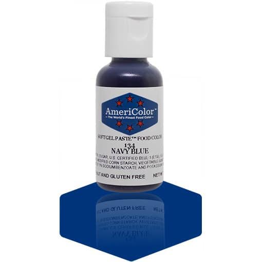 A bottle of AmeriColor Navy Blue soft gel paste food coloring with a white cap and blue label featuring red stars, placed on a dark navy blue reflective surface that mirrors the bottle.