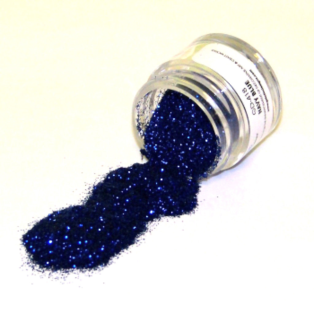 Small clear jar tipped on its side spilling navy blue glitter dust onto a white surface, with fine sparkling particles visible throughout.