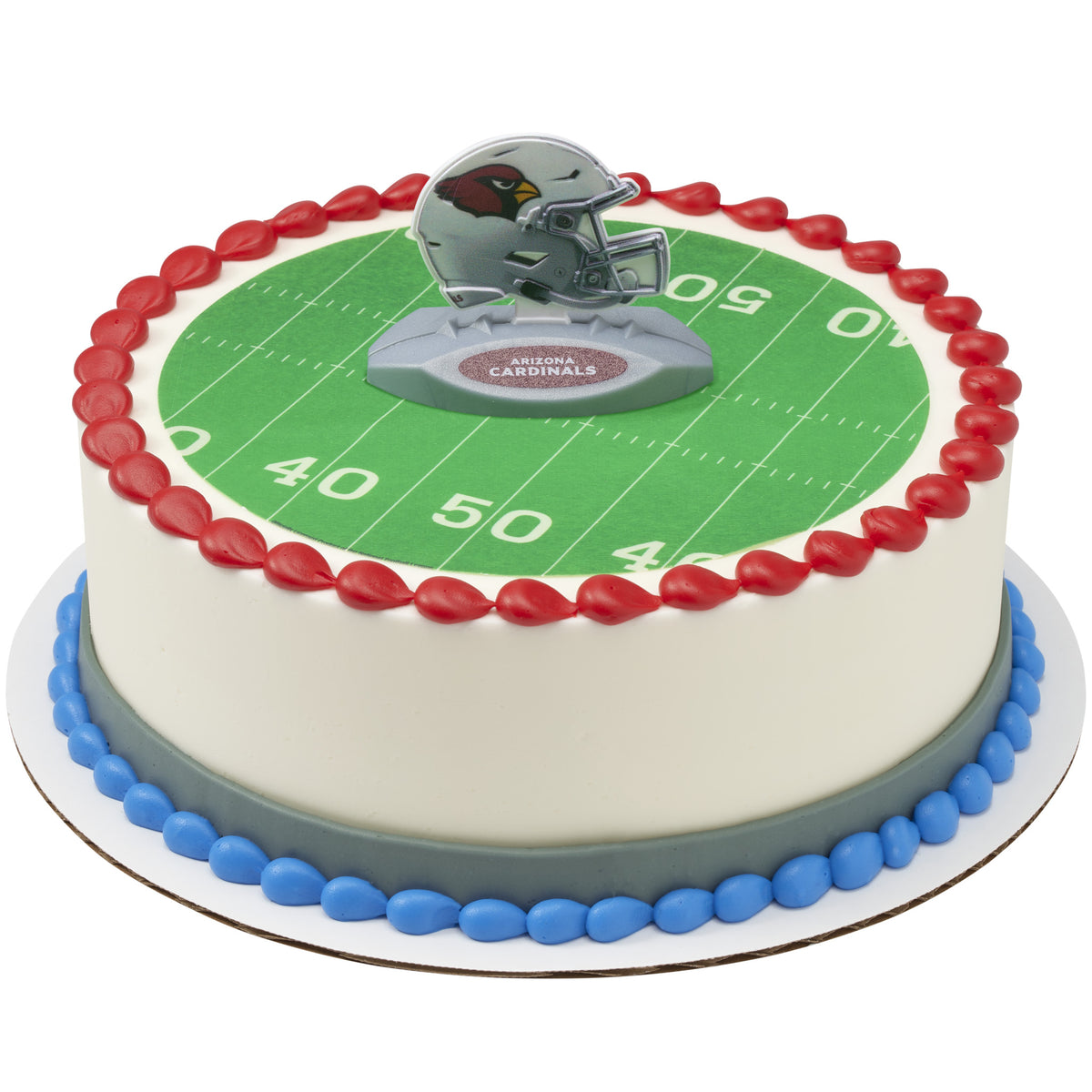 A round cake decorated to look like a football field, with a green yard-line surface, red piped border, blue base trim, and a small Arizona Cardinals helmet topper on top.