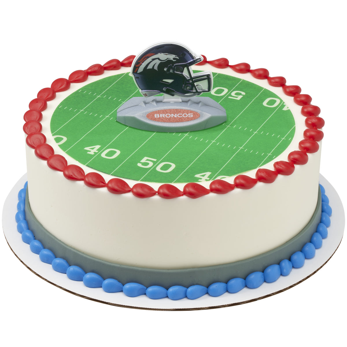 A round cake decorated with a green football field print, red piped border, blue base detail, and a Broncos helmet topper on top.