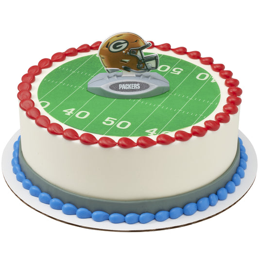 A round cake decorated with a green football field print, red piped border, blue base trim, and a Packers helmet topper on top.