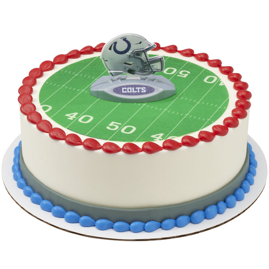 A round cake decorated to look like a football field, with a green turf top, red piped border, blue base trim, and a Colts helmet topper on a white background.