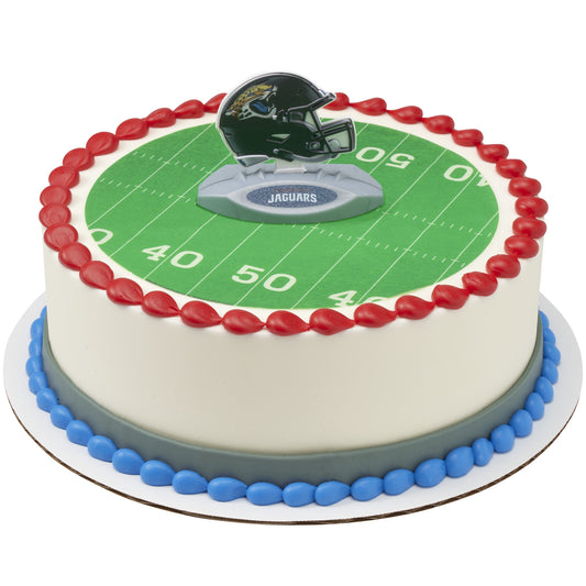 A round cake decorated with a green football field print, red piped border, blue base trim, and a Tampa Bay Buccaneers helmet topper on top.