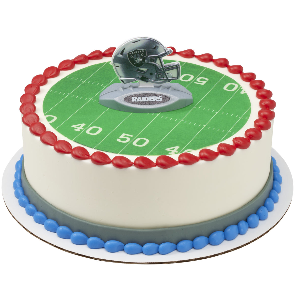 A round cake decorated with a green football field print, red piped border, blue base trim, and a Raiders helmet topper on top.