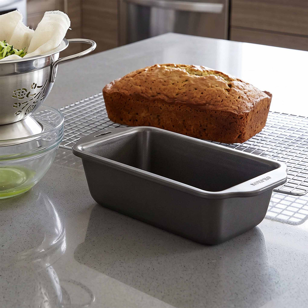 Nonstick loaf pan on a kitchen counter beside a freshly baked loaf cooling on a wire rack