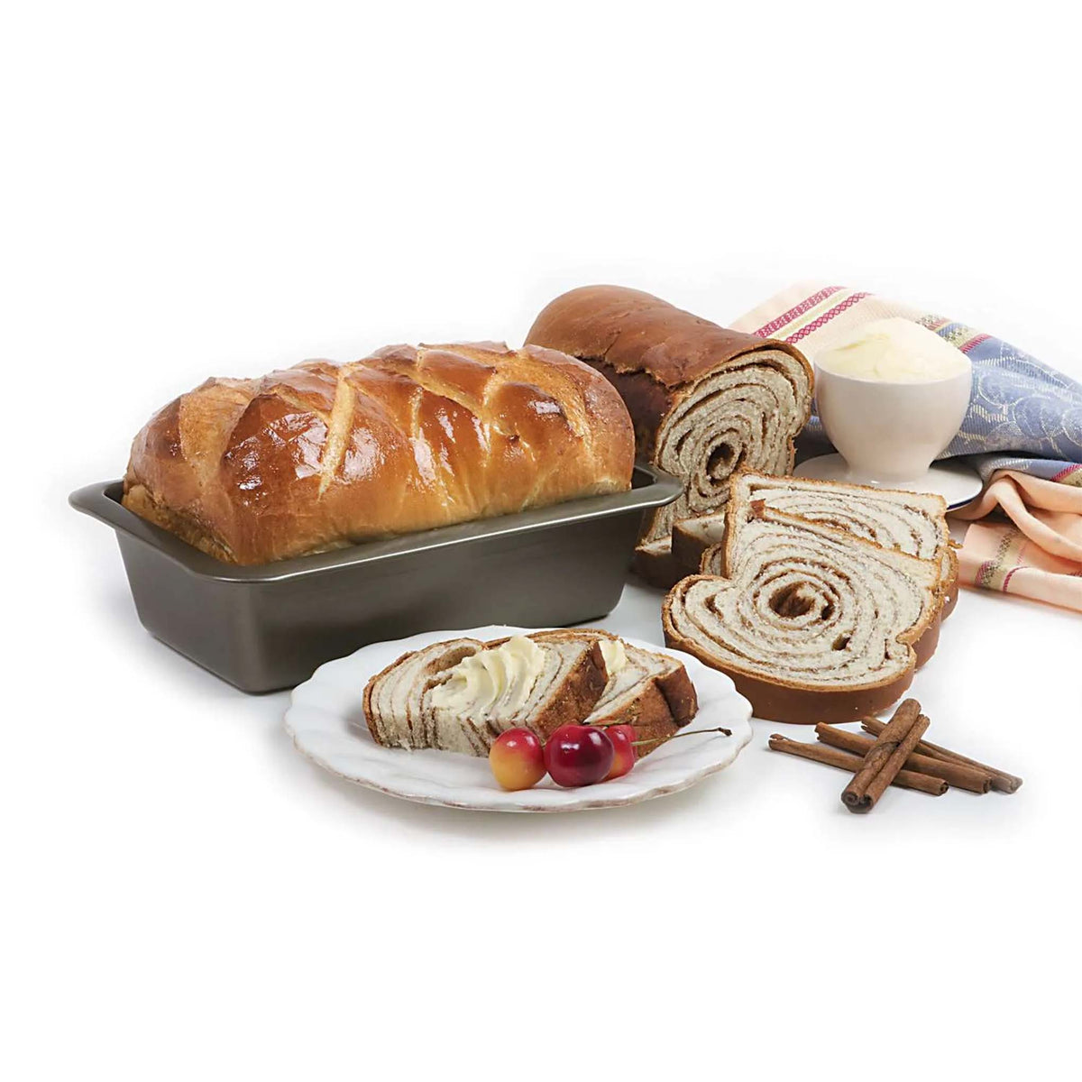 Nonstick loaf pan holding a baked loaf beside sliced cinnamon swirl bread and a cup of butter