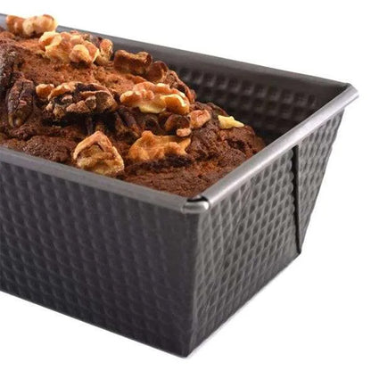 Close-up of a dark gray corrugated loaf pan filled with baked bread, showing a browned top with walnuts and visible tapered sides.