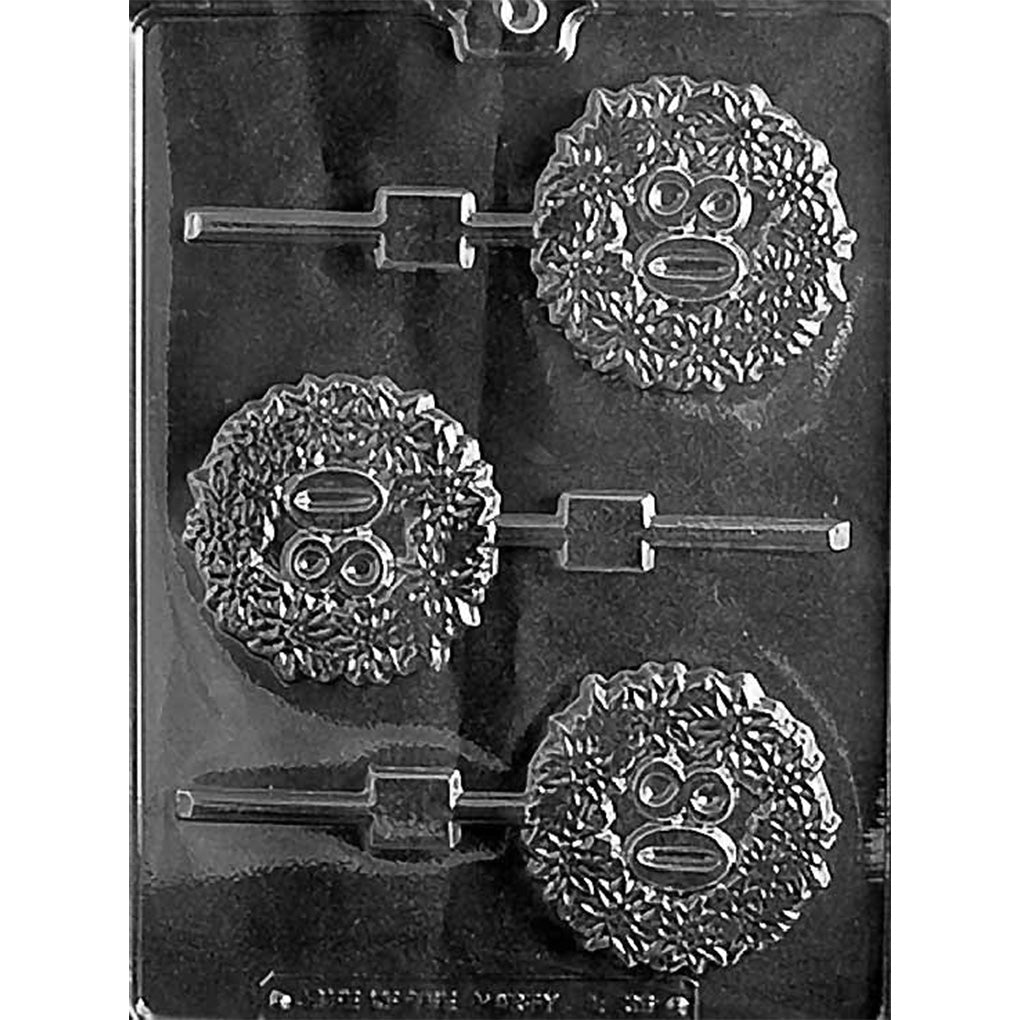 Clear plastic chocolate lollipop mold photographed on a black background with three round lollipop cavities featuring a textured face design with big eyes and a ruffled, furry-looking outline, plus stick channels.