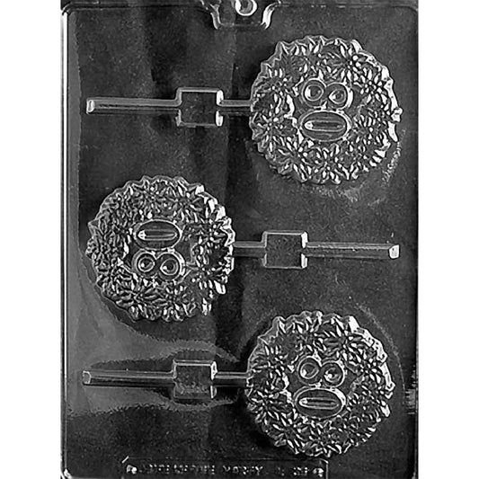 Clear plastic chocolate lollipop mold photographed on a black background with three round lollipop cavities featuring a textured face design with big eyes and a ruffled, furry-looking outline, plus stick channels.