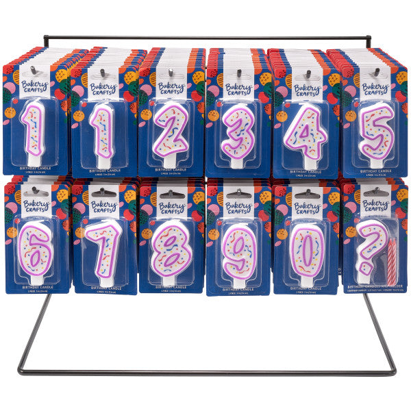 Display rack holding multiple packaged numeral birthday candles (0–9) with purple outlines and confetti centers on blue Bakery Crafts backing cards.