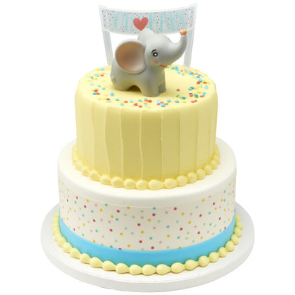 Two-tiered cake with pastel yellow and polka dot design, topped with a baby elephant figurine and “Oh Baby” banner.