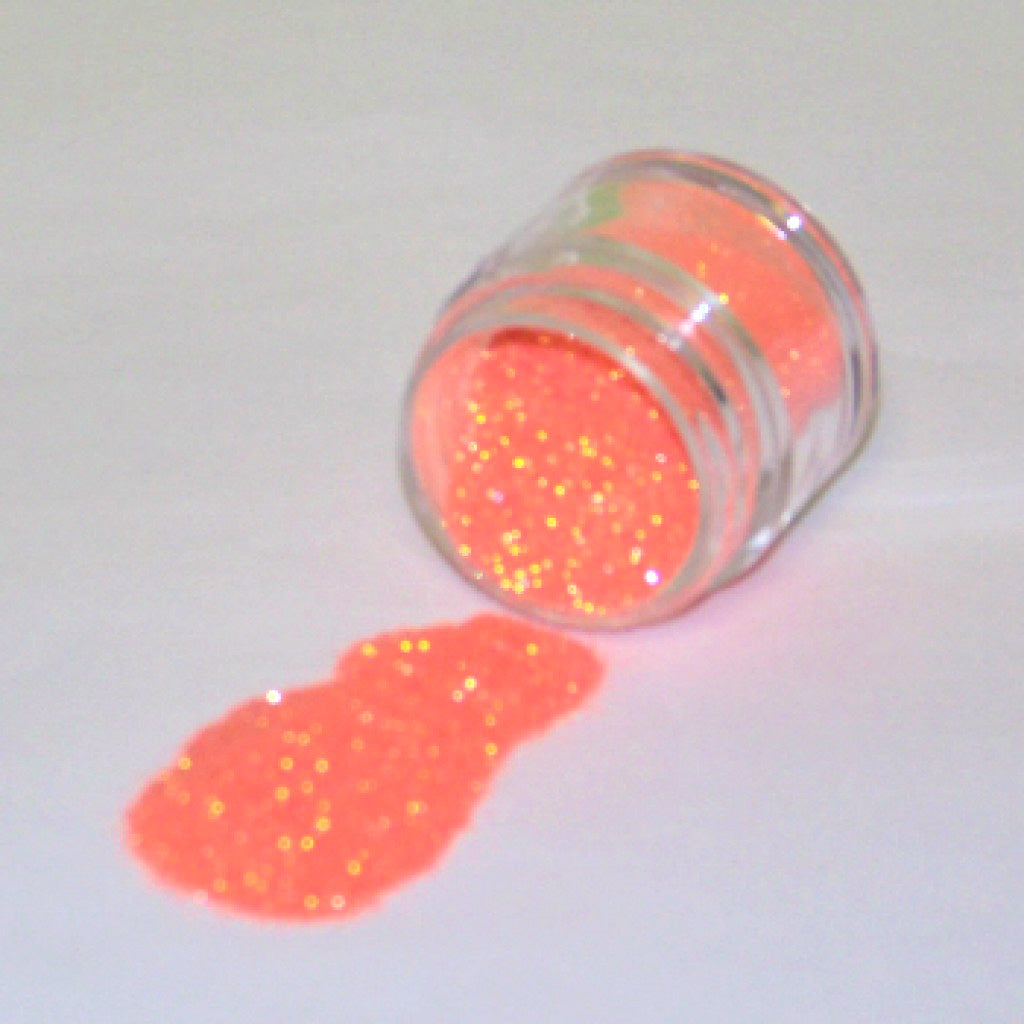 Small clear jar tipped on its side spilling bright orange glitter dust onto a white surface, showing fine sparkling particles with a vivid neon orange glow.