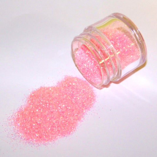 Small clear jar tipped on its side spilling pale osiana rose pink glitter dust onto a white surface, with fine shimmering particles creating a soft rosy sparkle.