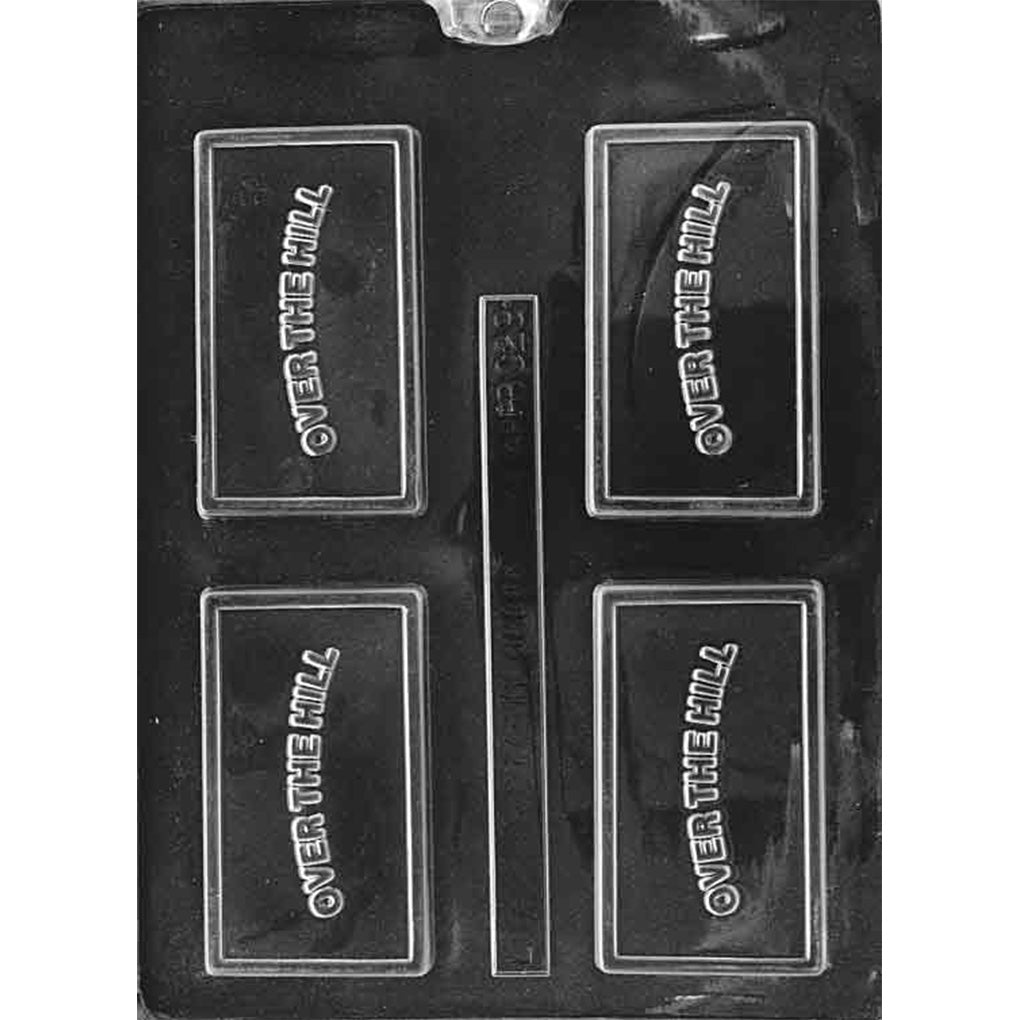 Clear plastic chocolate mold photographed on a dark background with four rectangular framed cavities, each featuring raised diagonal “OVER THE HILL” lettering.