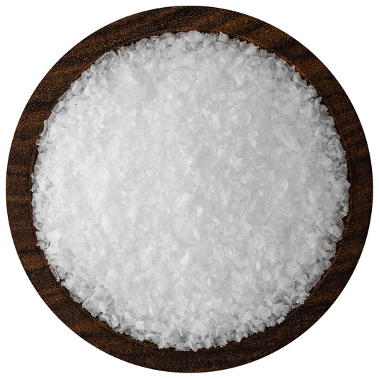 Overhead view of white kosher flake sea salt crystals piled in a round dark wooden bowl on a white background, showing thin, irregular flakes.