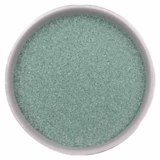 Top-down view of a white bowl filled with pastel green fine sanding sugar, showing tiny pale mint-green crystals with a soft shimmering texture.