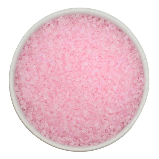 Top-down view of a white bowl filled with pastel pink coarse sanding sugar crystals, showing chunky sparkling granules in a soft blush-pink color.
