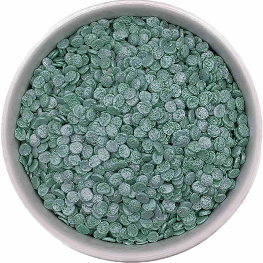 Top-down view of a bowl filled with green pearl confetti sprinkles, featuring flat, round edible discs with a shimmering pearlescent finish.