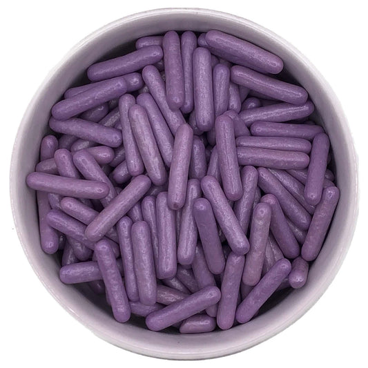 Top-down view of pearlized purple edible rod sprinkles in a bowl, featuring large, cylindrical shapes with a satin-like coating.