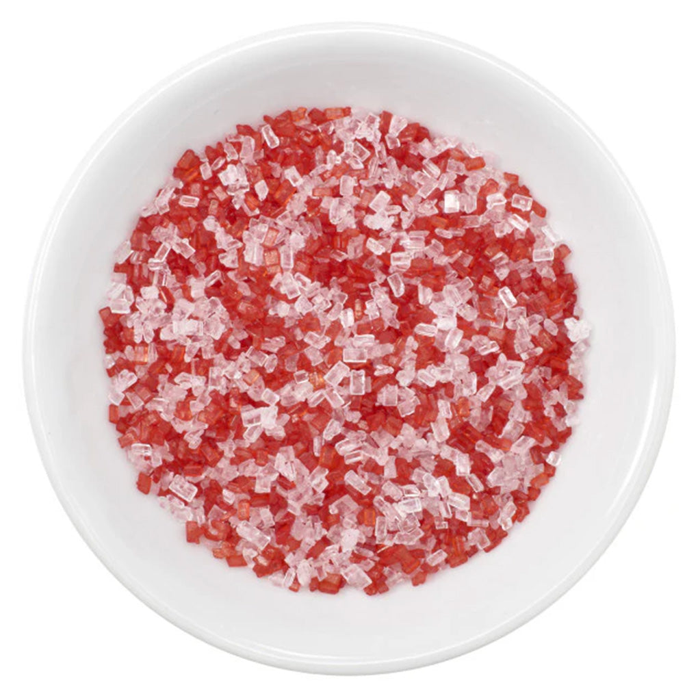 White bowl filled with peppermint sanding sugar blend made of red and clear rectangular sugar crystals, shown from above.