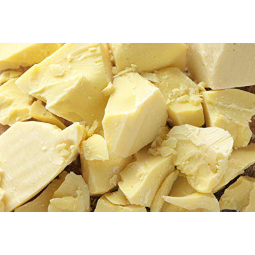Close-up of chunky pieces of pale yellow cocoa butter with rough, broken edges clustered together.