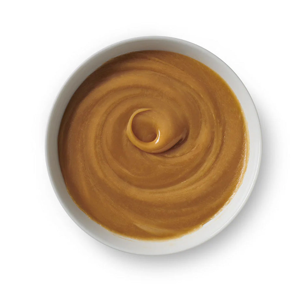 Top-down view of a white bowl filled with smooth, golden-brown liquid caramel swirled into a glossy spiral.