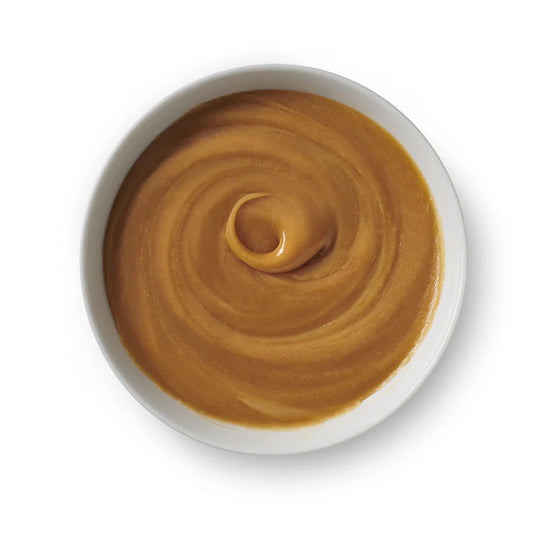Top-down view of a white bowl filled with smooth, golden-brown liquid caramel swirled into a glossy spiral.