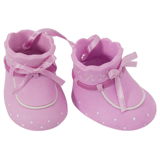 Close-up of pink baby booties with white detailing and ribbon bows, used as a cake topper decoration.
