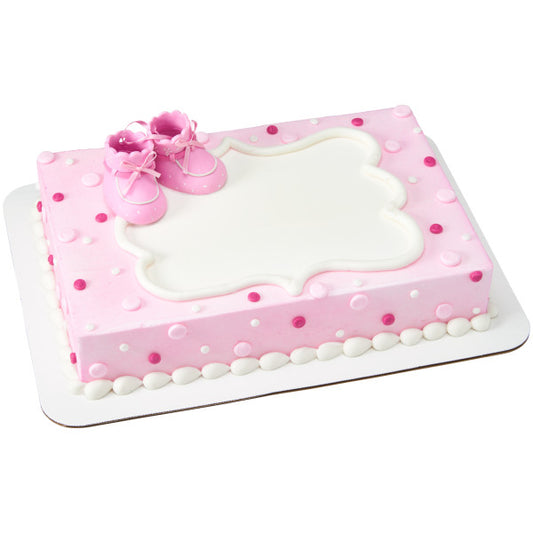 Rectangular baby shower cake decorated in pink and white with polka dots and topped with pink baby booties cake topper.