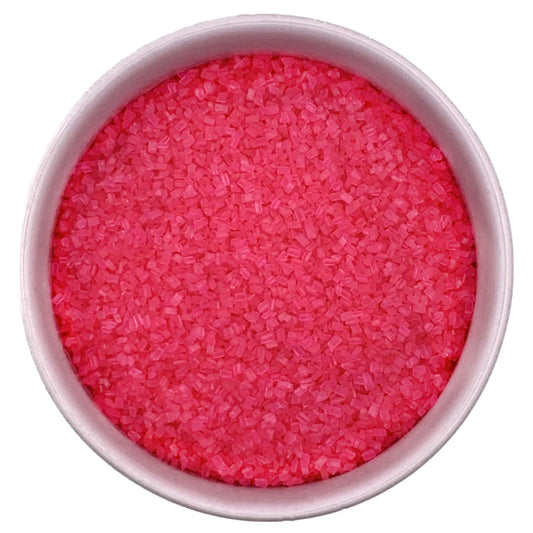 Top-down view of a white bowl filled with bright pink coarse sanding sugar crystals, showing chunky sparkling granules and a vivid candy-pink color.