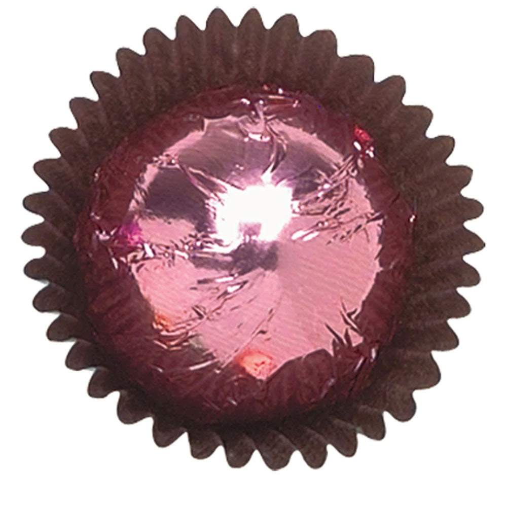 Close-up of a pink foil-wrapped chocolate in a dark brown paper candy cup, showing shiny pink metallic foil with reflective creases.