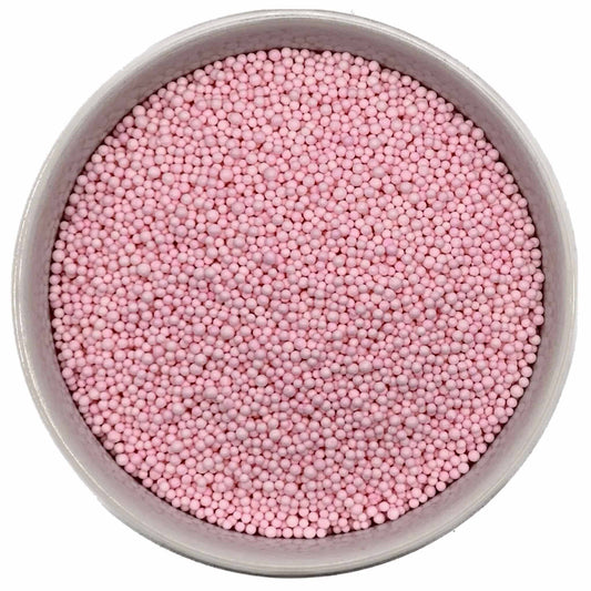 Top-down view of a round container filled with tiny pastel pink nonpareil sprinkles, showing small bead-shaped candy pieces tightly packed together.