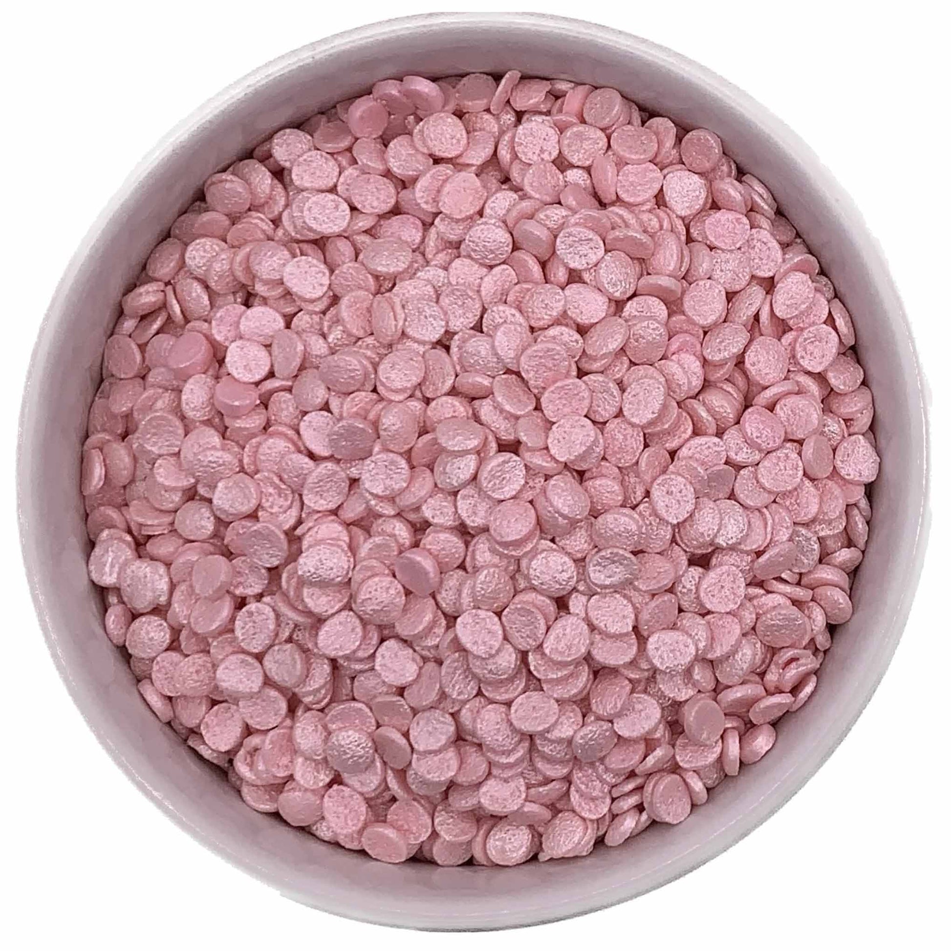 Top-down view of a bowl filled with pearlized pink confetti sprinkles, featuring small round edible discs with a soft shimmer finish.