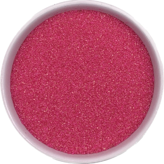 Fine pink sanding sugar poured into a white bowl, showing crystal texture and vibrant color for decorating.