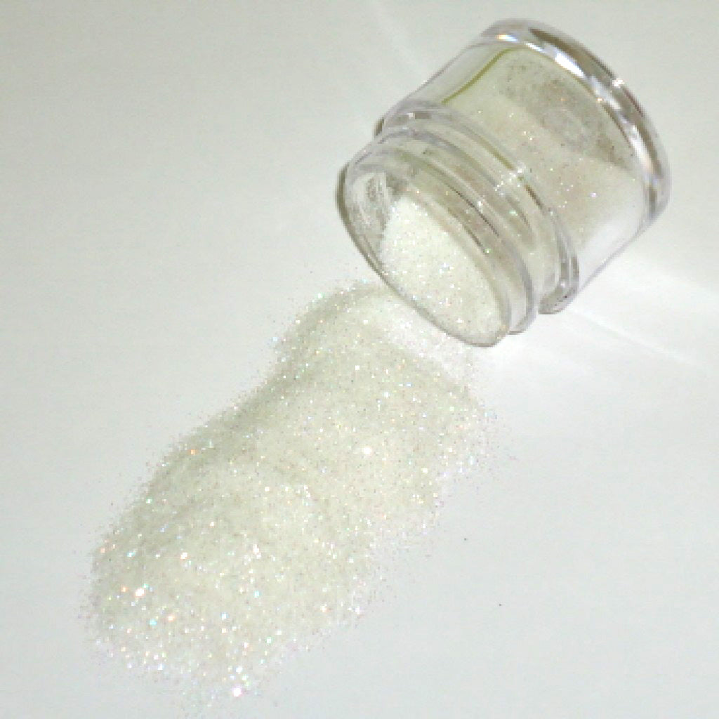 Small clear jar tipped on its side spilling Pixie Dust glitter dust onto a white surface, with fine iridescent particles creating a soft magical sparkle.
