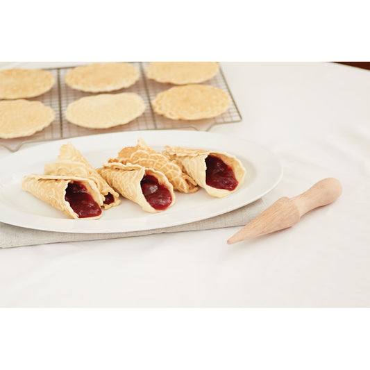 Wooden pizzelle cone roller beside crisp cone-shaped pastries filled with red fruit filling