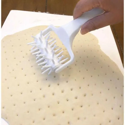 Hand using a white dough docker to pierce a sheet of dough.