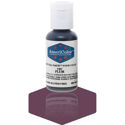 A bottle of AmeriColor Plum soft gel paste food coloring with a white cap, blue label, and red stars, standing on a rich plum-colored reflective surface that mirrors the bottle.