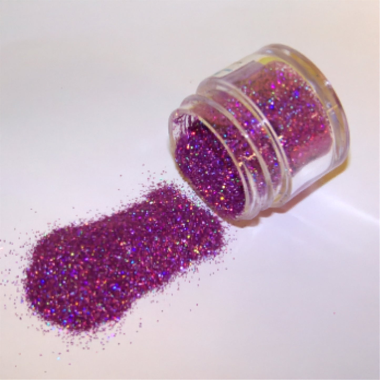 Jar of plum purple glitter dust spilled onto a white surface.