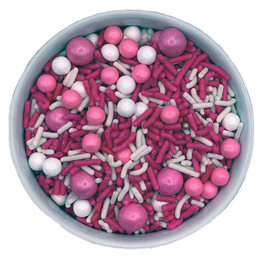 Princess sprinkle blend with pink and white jimmies, pink Sixlets, and assorted pink and white sugar pearls in a bowl