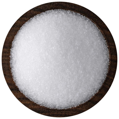 Overhead view of coarse white sea salt crystals piled in a round dark wooden bowl against a white background.
