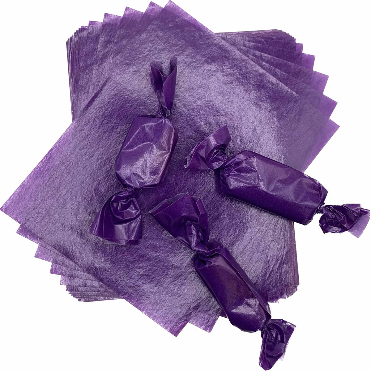 Three rectangular caramel pieces individually packaged in purple wax candy wrappers with twisted ends, displayed over a stack of 4" x 5" caramel wrapper sheets.