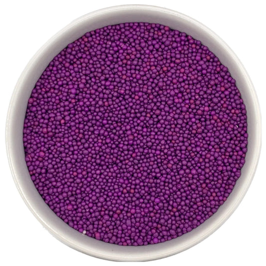 Top-down view of a white bowl filled with purple non-pareils, showing tiny round sprinkle beads in deep violet and magenta-purple shades.