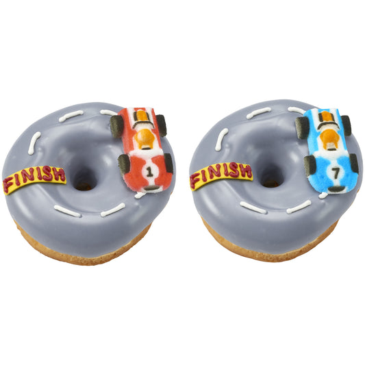 Two gray-glazed donuts decorated like racetracks with white icing lane marks and a yellow finish banner, each topped with a red or blue pressed sugar race car.