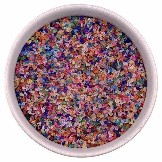 Top-down view of a white bowl filled with rainbow coarse sanding sugar crystals in mixed colors including pink, blue, green, orange, purple, and clear pieces.